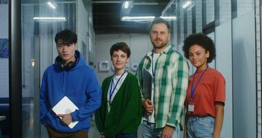 A group of handsome young people of different nationalities are smiling looking at the camera while standing in the modern office. Startup team, portrait. 4K , red komodo video