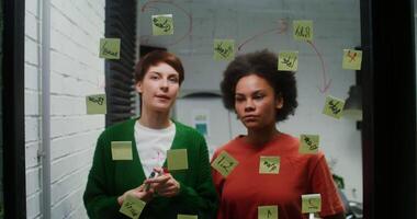 Young women rejoice while drawing a business development strategy for a startup on a glass board, working as pair in modern office. Shifting the focus of the from the whiteboard to female faces video