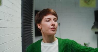 Young woman of European appearance is engaged in planning, drawing on a glass board with a marker and sticking stickers to it, working in a modern stylish office video