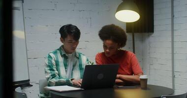 Young colleagues - an Asian man and an African American woman are working on a common project in a modern office, using a laptop and discussing work processes with concentration video