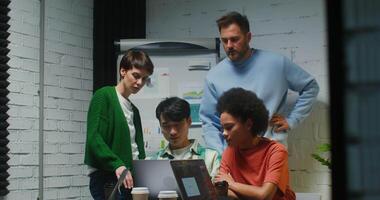 jovem colegas colhido por aí 1 computador portátil e discutir uma trabalhos projeto, olhando às a tela, trabalhando em uma comece dentro uma moderno à moda escritório video