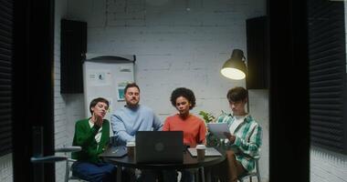 Group of young entrepreneurs of different nationalities watching presentation of new product on laptop, while sitting at table in modern stylish office video