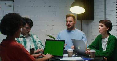 A group of young entrepreneurs of various nationalities are focused on creating a business plan for a startup, working on laptops with a green screen. Chroma key, copy space video