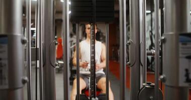 The heavy weights of a modern machine are lifted by the efforts of a young, athletic man working out in the gym. Close-up and vocus on the simulator, the man in the background is blurred video