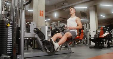 A healthy young man of European appearance is engaged in an exercise machine, shaking his chest muscles, lifting weights with his hands, sitting on a bench video
