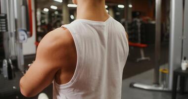 A young man of European appearance is engaged in a strength simulator, lifting heavy weights. Filming from behind, the man's face is not visible video