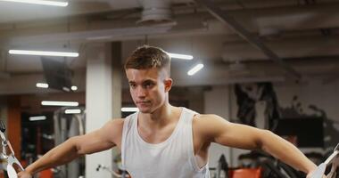 Young healthy man with athletic build of European appearance, with strong arms, training biceps while exercising on the exercise machine in a modern gym video