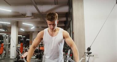 Front view of a young man of European appearance with the effort of lowering his arm and driving the exercise machine lifting weights. Classes in a modern gym for the muscles of the arms video