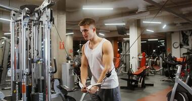 A young man of european appearance is concentratedly lifting weights, exercising on a modern simulator in a well-equipped gym, doing exercises on the muscles of the arms video