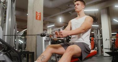 A sportive young man of European appearance is engaged in a simulator for exercises on the muscles of the chest, lifting weights with his hands, sitting on a bench in a modern gym video
