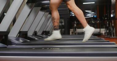 Close-up footage of a young man of European appearance running on a treadmill in the gym, the frame moving from the man's legs to his face video