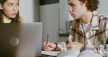 Young students work in pairs, using a laptop and making notes in a notebook while sitting at the table in the kitchen. Online training, teamwork on a project video