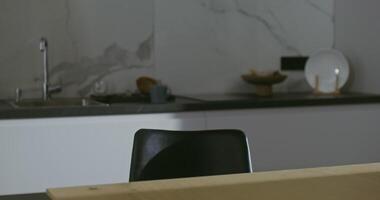 Young male european appearance, with a bristle on his face, sits down the kitchen table, not taking off view from a mobile phone and sitting continues to texting on mobile with concentrated view video