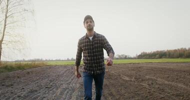 A young black-haired man of European appearance with a beard, walks through an agricultural field to a tractor and gets behind the wheel and starts the car to continue working video