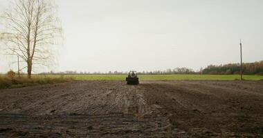 A male tractor driver drives an agricultural tractor plowing a small field on a fine autumn day. Filming from afar video