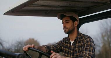 A young male farmer of European appearance rides an agricultural tractor with an open cabin, plowing a field on an autumn day, videography of the details of the work close-up video