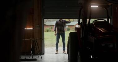 The garage door slowly opens and a young man of European appearance comes inside, inspecting the tractor parked there and getting behind the wheel. Filming from the darkness of the garage video
