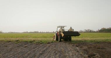 A young European farmer drives into a field after turning an agricultural tractor, starting to plow a new strip with a plow located at the rear of the machine video