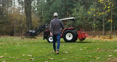 Young male farmer getting ready to start work in the field on an autumn day, getting into a modern agricultural tractor and starting it video