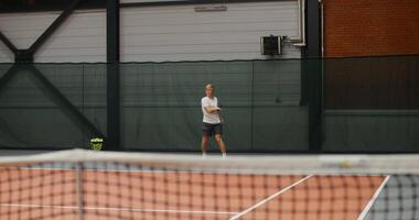 A young man of European appearance, dressed in a stylish sports uniform, hits the ball after the ball with force, hitting it with a racket and actively bouncing video