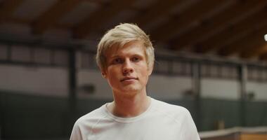 Close-up face of young blond male throws a tennis racket behind his head in indoor tennis court, and smiling slightly video