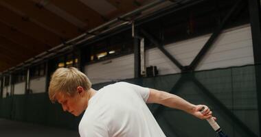 A young man of European appearance throws and hits the ball with a racket playing tennis. Close-up filming from the side video