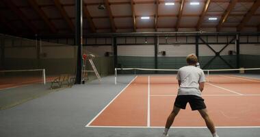 A young man of European appearance is intently waiting for the first ball of his opponent who starts the tennis set and the game begins. Filming from behind a man video