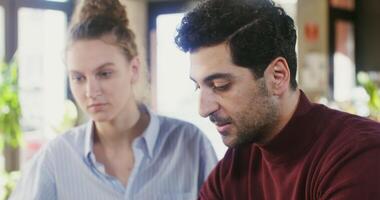 Two young people - a man and a woman are looking at a laptop screen and talking, working on a common project while sitting at a table in a modern coffee shop video