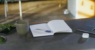 a aberto caderno com uma caneta mentira em a mesa Próximo para uma computador portátil, uma caneca e uma caso para sem fio fones de ouvido, fechar-se, não pessoas. local de trabalho para controlo remoto trabalhos video