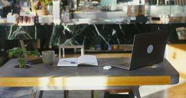 Workplace for remote work in a modern stylish coffee shop. An open laptop and a notepad lie on the table in the coworking space video