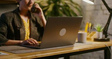 Young beautiful businesswoman of European appearance, with short hair talking on a mobile phone while sitting in front of an open laptop at a table in a modern stylish office. video