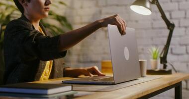 Young beautiful woman of European appearance opens the lid of a laptop and starts typing while working in a modern stylish office, under the light of a table lamp video