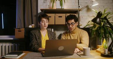 Two young colleagues - a man and a woman working on a laptop while sitting at the table in the office and achieving success rejoice at the profit, banknotes fall from the ceiling in the office video