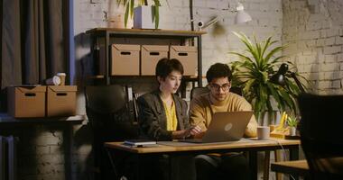 Two stylishly dressed young people - a man and a woman working on a laptop in the office and achieving success rejoice at the profit, banknotes fall from the ceiling in the office video