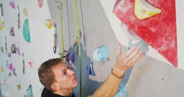 A young man of European appearance climbs up the artificial surface of the climbing wall, striving for the top. Sports lifestyle, leisure and hobbies video
