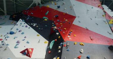 A young man of European appearance, equipped with climbing harnesses, slowly and carefully climbs up a climbing wall with many irregularities and angles video