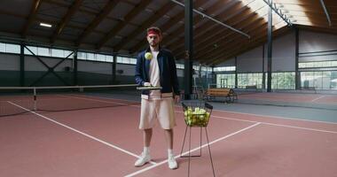 A young man of European appearance stuffs a tennis ball with a racket, with a serious look and looks at the camera video