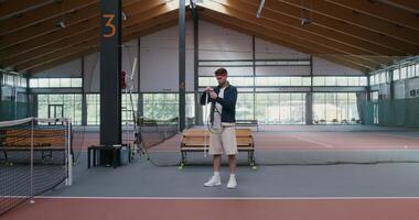 A young man of European appearance wraps the handle of a tennis racket with a special tape, for better grip on the hand, preparing for a tennis match video