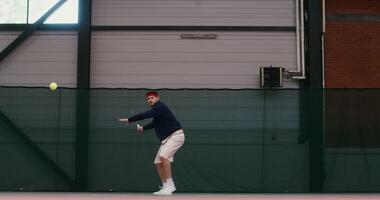 A young man of European appearance plays big tennis, hitting the ball with a racket over and over again, bouncing with each racket hit, front view video