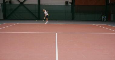 A young male tennis player of European appearance prepares to throw a tennis ball, stuffing it with his hand from the floor covering, then makes a strong hit with a racket video