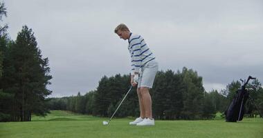 Handsome blond young man playing golf on a large field alone. Ball hitting with a golf club, dynamic action. Stylish golf apparel and equipment video