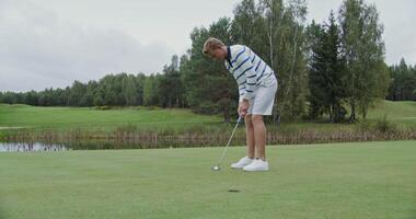 A young man of European appearance in stylish sportswear slowly launches a golf ball into the hole, hitting it with a club, but the ball misses the target, rolling to the side video