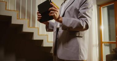 A woman realtor takes pictures of a modern light two-story house on a tablet, making an overview of the premises for sale video