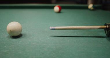 The cue is aiming at the white ball lying on the billiard table, close-up, the camera repeats the movements of the cue video