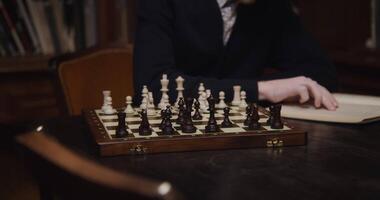 en ung man av europeisk utseende, klädd i en företag kostym, är studerar med koncentration till spela schack ensam, använder sig av en lärobok, Sammanträde på en tabell i de bibliotek, närbild video