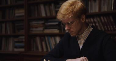 A European-looking man with glasses looks down at the chessboard with concentration, thinking before making a move video