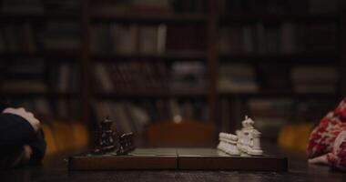 A man and a woman are preparing for a chess game, sitting opposite each other at a table in the library, a close-up of a chessboard with only lined pieces video