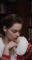A young beautiful girl of European appearance with freckles and in large earrings is thinking intently, resting her chin with her hands and looking down at the table, close-up, vertical video