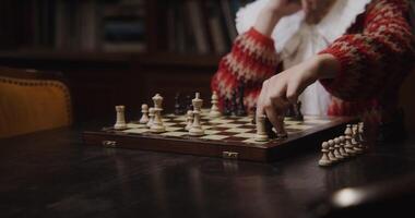 A young woman of European appearance plays a chess game alone, thinking for a long time between moves and turning the board over, changing color, sitting at a long table in the library video