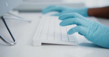 A doctor in disposable blue gloves is typing on a computer keyboard in a snow-white office, a close-up shot video